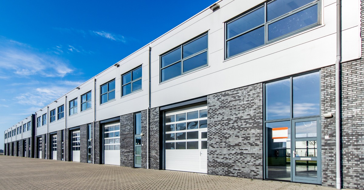 Commercial warehouse building with brick lower walls, multiple bay doors, glass entry doors, and second-story windows.