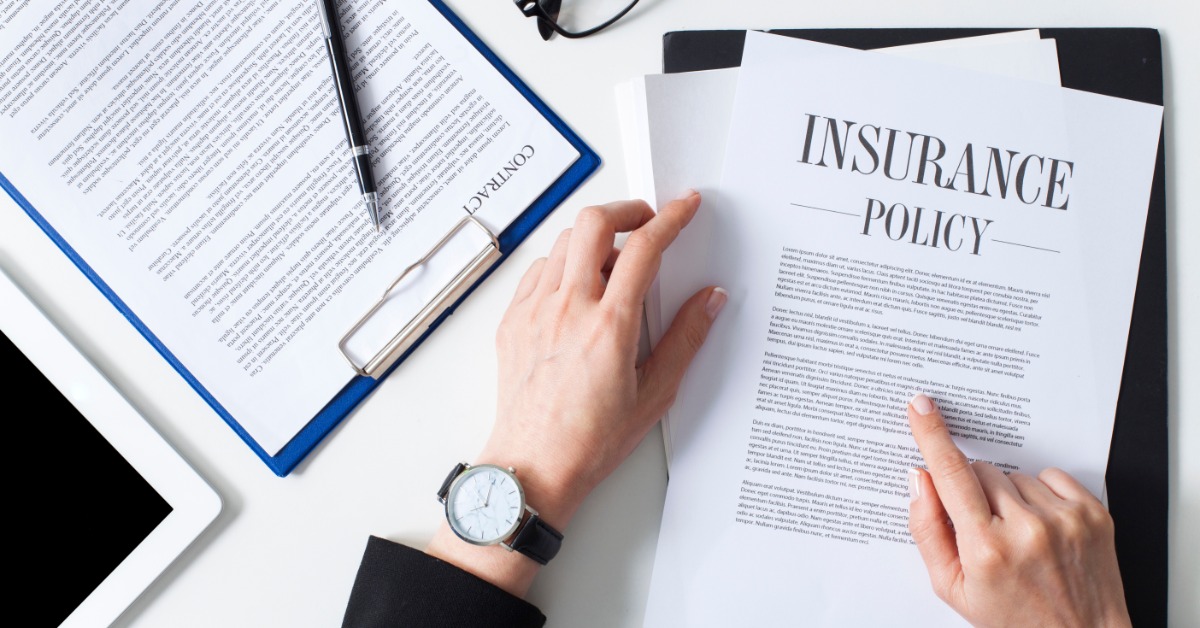 An overhead view of hands holding papers titled "Insurance Policy." A pen, glasses, and another document are nearby.