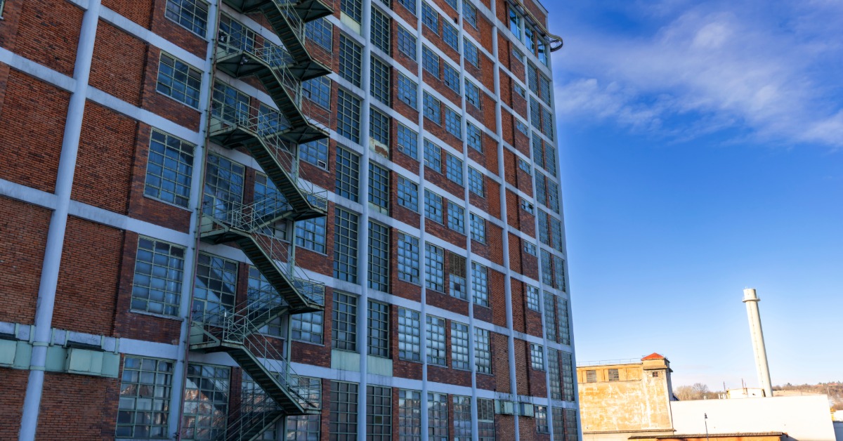The exterior of a historic industrial brick building with a large fire escape and industrial windows on a sunny day.