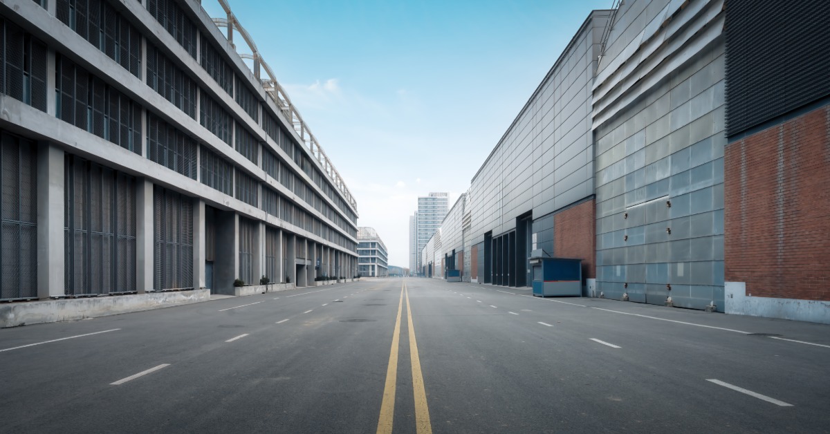 A view from the middle of an empty, five-lane road with developments and buildings on each side during the day.