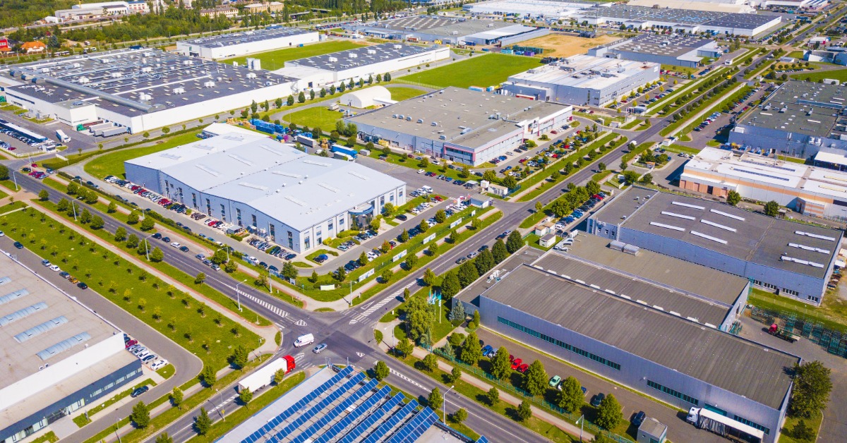 Aerial view of an industrial park with multiple large warehouses, wide roads, parking lots, and landscaped green areas.